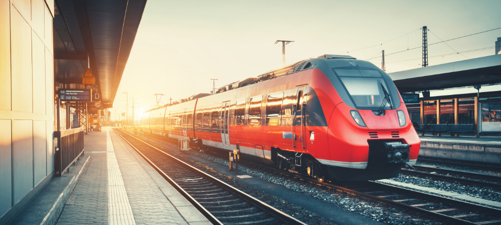 Beautiful railway station with modern high speed red commuter train at colorful sunset. Railroad with vintage toning. Train at railway platform. Industrial concept. Railway tourism